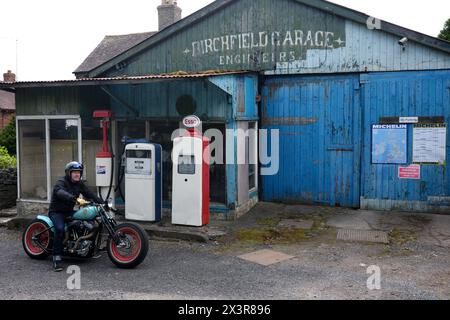 Motocycliste sur une moto construite sur mesure dans un vieux garage désaffecté à Much Wenlock, Shropshire Banque D'Images