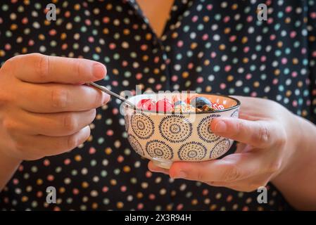 Petit bol de yaourt frais avec granola, baies d'été mélangées, banane et kiwi mangé avec une cuillère Banque D'Images