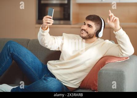 Jeune homme souriant dans une tenue décontractée appréciant la musique avec casque Banque D'Images