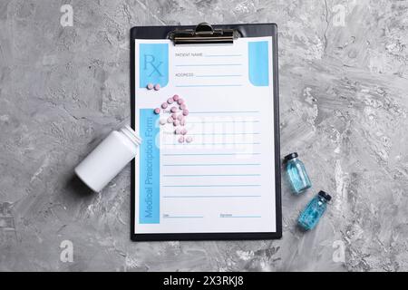 Formulaire de prescription médicale avec champs vides, pots de pilules et liquide sur table texturée grise, pose à plat Banque D'Images