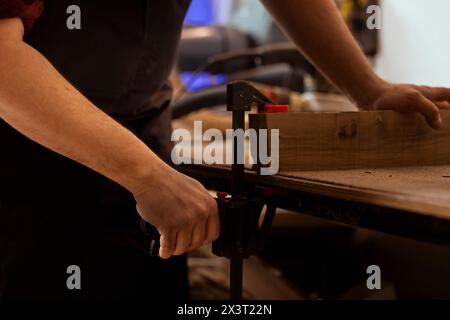 Menuisier utilisant un étau d'établi pour maintenir le bloc de bois, commencer l'assemblage des meubles dans l'atelier, plan rapproché. Artisan dans la menuiserie à l'aide de l'outil étau pour serrer le morceau de bois avant de le sculpter Banque D'Images