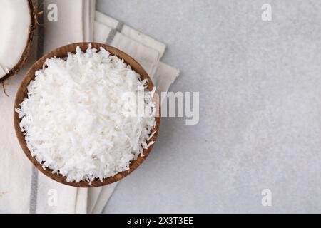 Flocons de noix de coco dans un bol sur une table gris clair, vue de dessus. Espace pour le texte Banque D'Images