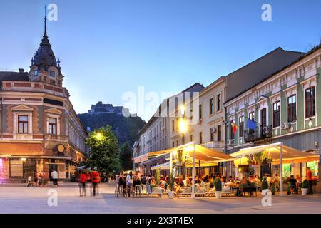 Scène nocturne à Deva, comté de Hunedoara, Roumanie à Piata Unirii (place de l'Union), avec la forteresse de Deva qui se profile au sommet de la colline en arrière-plan. Banque D'Images