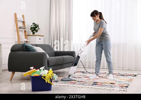Heureuse jeune femme au foyer aspirant tapis à la maison Banque D'Images
