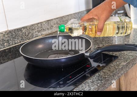 main mettre l'huile dans une poêle sur une cuisinière à induction dans la cuisine Banque D'Images