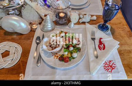 Mélange de fruits de mer et salade Caprese avec tomates cerises, mozzarella, basilic et roquette sur une belle assiette avec une table décorée en coquillage. Banque D'Images