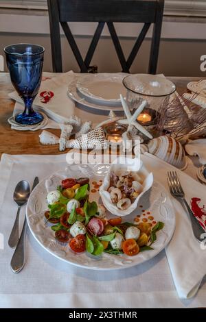 Mélange de fruits de mer et salade Caprese avec tomates cerises, mozzarella, basilic et roquette sur une belle assiette avec une table décorée en coquillage. Banque D'Images