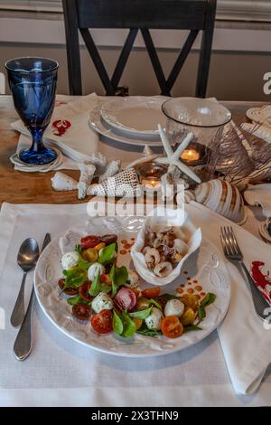 Mélange de fruits de mer et salade Caprese avec tomates cerises, mozzarella, basilic et roquette sur une belle assiette avec une table décorée en coquillage. Banque D'Images