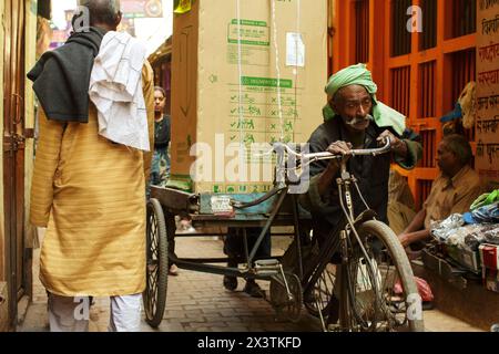 Homme âgé poussant un transporteur de marchandises à vélo chargé d'un réfrigérateur dans une ruelle à Varanasi, en Inde. Banque D'Images