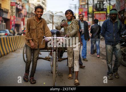 Deux jeunes hommes poussant un bon porteur de vélo le long d'une route à Varanasi, en Inde. Banque D'Images