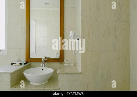 Salle de bains de luxe avec un lavabo en céramique blanche, robinet et un miroir avec une étagère au-dessus. Un sèche-cheveux est placé sur l'étagère. Propre, classique et bien-ma Banque D'Images