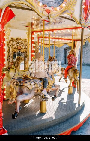 Les petites filles montent un cheval jouet sur un carrousel coloré. Vue arrière Banque D'Images