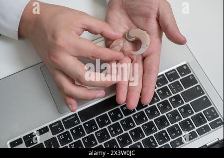 Gros plan des mains d'un homme avec une prothèse auditive près d'un ordinateur portable. Banque D'Images