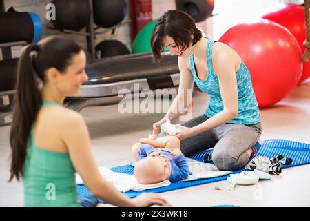 Mère changeant sa couche pendant un cours d'exercice en groupe. Les mamans restent actives, s'entraînent avec bébé dans la salle de gym, se lient. Banque D'Images