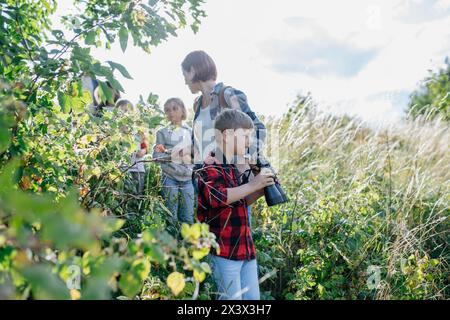 Jeunes élèves apprenant la nature, l'écosystème forestier pendant la classe d'enseignement sur le terrain de biologie, écolier observant la faune avec des bionoculaires. Dédié Banque D'Images