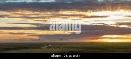 Un beau coucher de soleil sur une vaste plaine vide. Le ciel est rempli de nuages et le soleil se couche, projetant une lueur chaude sur le paysage Banque D'Images