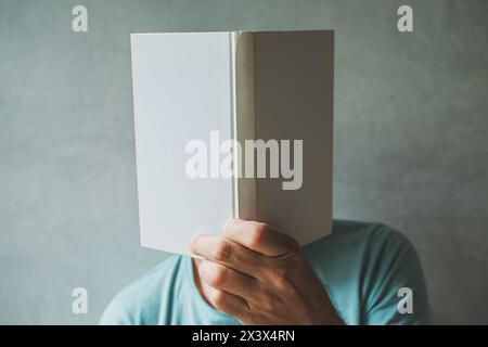 Lecteur masculin cachant son visage derrière le livre blanc maquette, mise au point sélective Banque D'Images