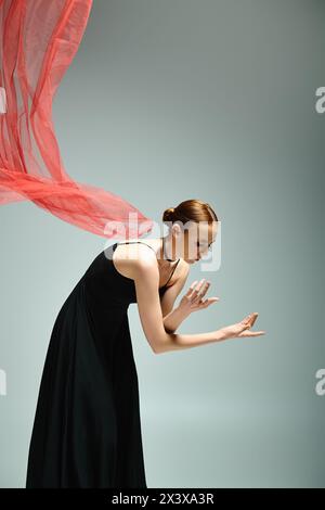 Une jeune et belle ballerine danse gracieusement dans une robe noire et un châle rouge vif. Banque D'Images