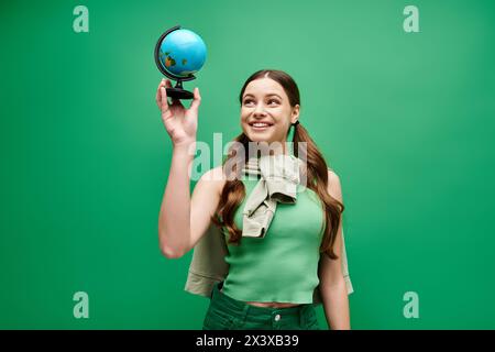 Une jeune belle femme dans sa vingtaine d'années tient délicatement un globe bleu fascinant dans un cadre de studio sur vert. Banque D'Images