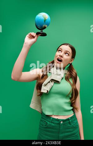 Une jeune belle femme dans la vingtaine portant une chemise verte, tenant un globe bleu dans un cadre de studio. Banque D'Images