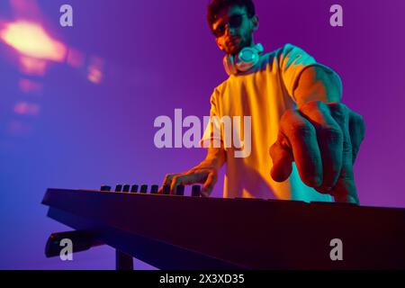 Young Man, perdu dans le rythme, mixe des pistes sur un mixeur DJ, alimentant l'énergie de la foule sur fond violet rose dégradé dans la lumière néon Banque D'Images