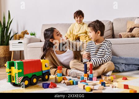 Une jeune mère asiatique assise sur le sol, jouant joyeusement avec ses petits fils dans le salon confortable de leur maison. Banque D'Images