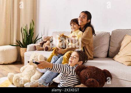 Une jeune mère asiatique et ses petits fils sont assis sur un canapé entouré d'animaux en peluche, créant une scène chaleureuse et intime. Banque D'Images