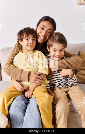 Une jeune mère asiatique est assise sur un canapé, entourée de ses deux petits fils énergiques, dans leur salon confortable à la maison. Banque D'Images