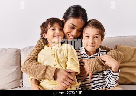 Une jeune mère asiatique profite d'un moment douillet assise sur le canapé avec ses deux petits fils dans le salon. Banque D'Images