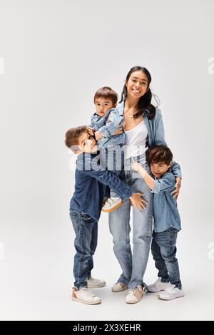 Une jeune mère asiatique posant avec ses petits fils, tous habillés en denim, capturant un moment réconfortant dans un studio gris. Banque D'Images