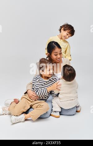 Une jeune mère asiatique est assise sur le sol avec ses enfants, créant un moment chaleureux en famille dans un cadre de studio. Banque D'Images