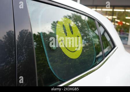 Pare-soleil jaune à visage souriant sur la vitre arrière de la voiture blanche Banque D'Images