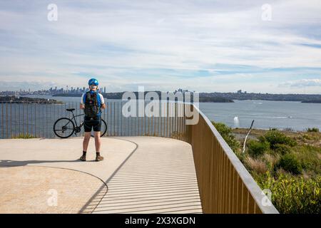 Cycliste masculin d'âge moyen au belvédère de Burragula sur Fairfax Track North Head, profite de la vue sur le port de Sydney et le paysage urbain de Sydney, Nouvelle-Galles du Sud, Australie Banque D'Images