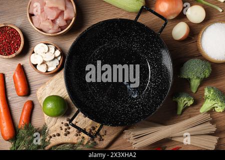 Wok en fer vide entouré d'ingrédients bruts sur une table en bois, plat Banque D'Images