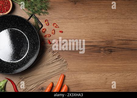 Wok en fer vide entouré d'ingrédients bruts sur une table en bois, plat. Espace pour le texte Banque D'Images