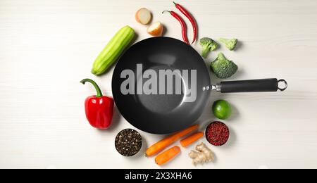 Wok en fer vide entouré d'ingrédients bruts sur une table en bois blanc, plat Banque D'Images