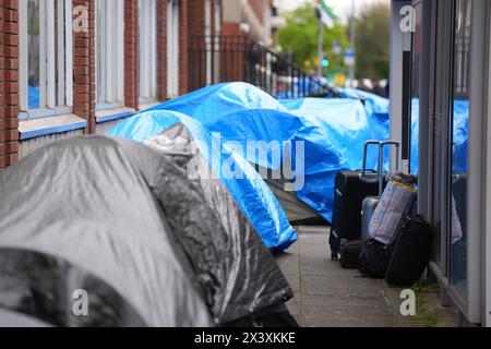 Des gens passant devant des tentes abritant des demandeurs d'asile près du Bureau de la protection internationale, à Dublin. Les allégations selon lesquelles la majorité des demandeurs d'asile entrant en Irlande avaient franchi la frontière depuis l'Irlande du Nord ont été interrogées par des organisations de défense des droits de l'homme et de réfugiés. La ministre irlandaise de la Justice Helen McEntee a affirmé la semaine dernière que le nombre de demandeurs d'asile traversant l'Irlande du Nord pour entrer dans l'État est maintenant "supérieur à 80%" suite à un changement dans les schémas migratoires ces derniers mois. Date de la photo : lundi 29 avril 2024. Banque D'Images