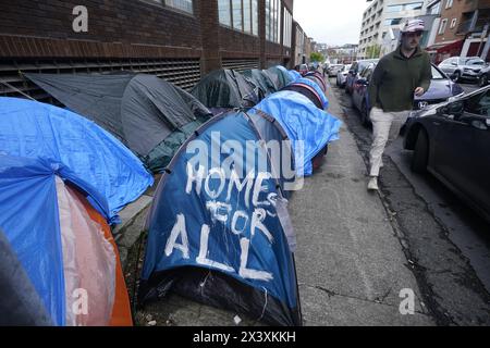 Des gens passant devant des tentes abritant des demandeurs d'asile près du Bureau de la protection internationale, à Dublin. Les allégations selon lesquelles la majorité des demandeurs d'asile entrant en Irlande avaient franchi la frontière depuis l'Irlande du Nord ont été interrogées par des organisations de défense des droits de l'homme et de réfugiés. La ministre irlandaise de la Justice Helen McEntee a affirmé la semaine dernière que le nombre de demandeurs d'asile traversant l'Irlande du Nord pour entrer dans l'État est maintenant "supérieur à 80%" suite à un changement dans les schémas migratoires ces derniers mois. Date de la photo : lundi 29 avril 2024. Banque D'Images