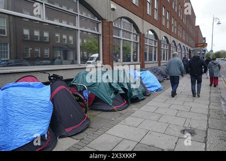 Des gens passant devant des tentes abritant des demandeurs d'asile près du Bureau de la protection internationale, à Dublin. Les allégations selon lesquelles la majorité des demandeurs d'asile entrant en Irlande avaient franchi la frontière depuis l'Irlande du Nord ont été interrogées par des organisations de défense des droits de l'homme et de réfugiés. La ministre irlandaise de la Justice Helen McEntee a affirmé la semaine dernière que le nombre de demandeurs d'asile traversant l'Irlande du Nord pour entrer dans l'État est maintenant "supérieur à 80%" suite à un changement dans les schémas migratoires ces derniers mois. Date de la photo : lundi 29 avril 2024. Banque D'Images