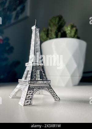 Un modèle isolé de Tour Eiffel argenté sur un fond blanc avec un fond flou d'un cactus dans un pot blanc. Banque D'Images