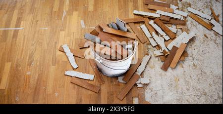 Artisan en vêtements de travail enlève le parquet et remplit les seaux avec les lattes en bois pendant le processus de rénovation de la maison. Banque D'Images