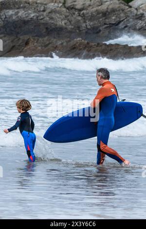 Un père et son jeune fils pataugant dans la mer avec une planche de surf à Fistral à Newquay en Cornouailles au Royaume-Uni. Banque D'Images