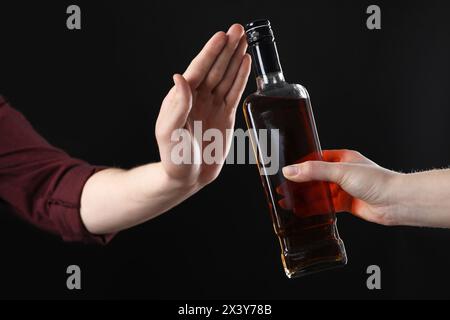 Alcoolisme. Femme refusant la bouteille de whisky sur fond noir, gros plan Banque D'Images