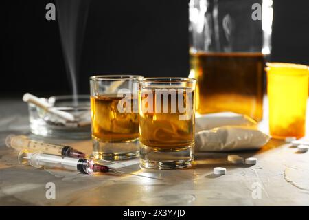 Alcoolisme et toxicomanie. Whisky dans des verres, seringues, pilules et cocaïne sur table grise Banque D'Images