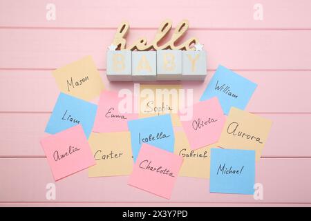 Cubes avec phrase Hello Baby et autocollants en papier avec différents noms sur fond de bois rose, pose à plat. Choisir le nom du bébé Banque D'Images