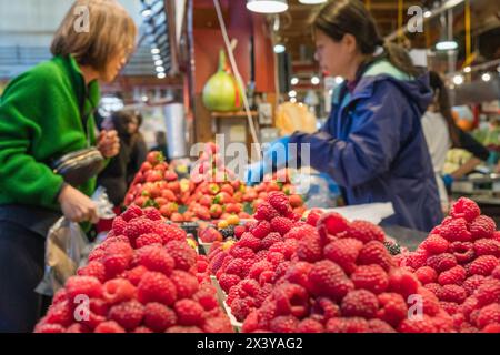 Le 10 août 2023-Vancouver, C.-B., Canada-gros plan sur des boîtes de baies biologiques fraîches colorées exposées dans un marché agricole avec des gens qui magasinent à l'arrière-plan. Banque D'Images