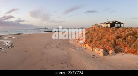 Une cabane de plage isolée avec une vue sur la mer sur les dunes de sable de Northumbrian surplombant Embleton Bay et Dunstanburgh Castle au coucher du soleil Banque D'Images