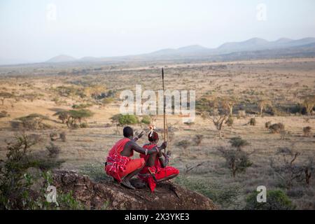 Deux guerriers Massaï vêtus de vêtements traditionnels se tiennent sur un rocher à la recherche d'animaux sur le plateau de Laikipia, au Kenya. Banque D'Images