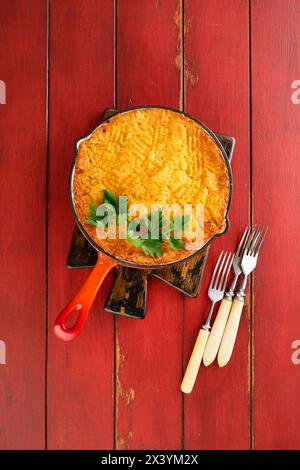 Shepherd's Pie avec du bœuf haché, des pois, des carottes, des oignons, des pommes de terre et du fromage sur fond de bois ancien dans une casserole en fonte. Plat traditionnel britannique fait maison Banque D'Images