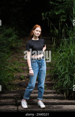 Fille de douze ans aux cheveux rouges avec des taches de rousseur posant debout sur toute la longueur avec un fond de bokeh nature, Belgique Banque D'Images